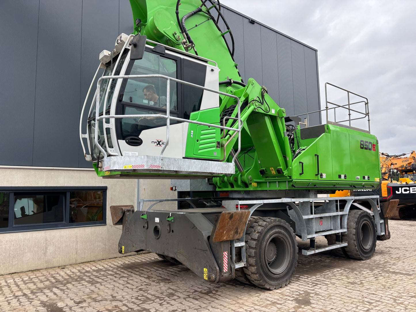 Sennebogen material handling machine cab with operators landing and upper railing package on solid tires with outriggers
